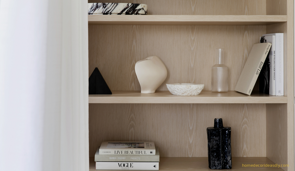 A curated oak shelf displaying carefully chosen luxury decorative objects including a sculptural ceramic vase, marble bowl, and glass bottle showing the thoughtful process of selecting home decor that earns its place.
