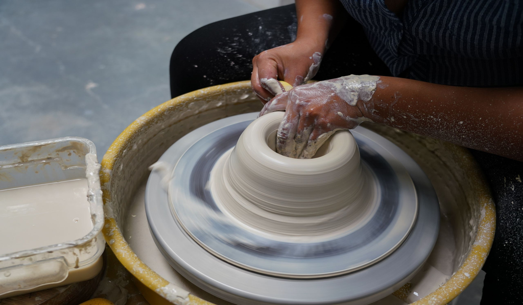 Close-up of a potter's hands shaping wet clay on a spinning pottery wheel, showing the handmade process and throwing rings that distinguish real home decor items handmade from machine-made copies.