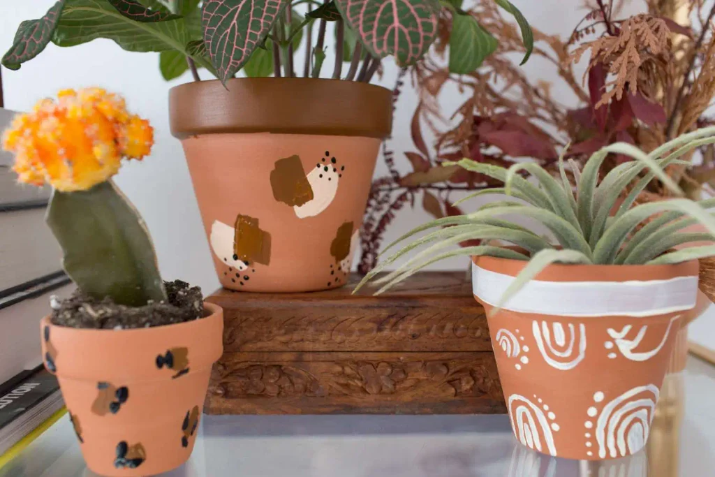 Handmade decor painted terracotta pots with cactus and plants on wooden surface