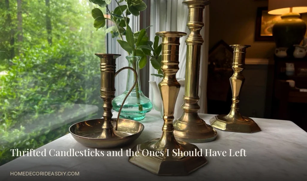 Thrifted vintage brass candlesticks of mismatched heights on a marble table by a window..