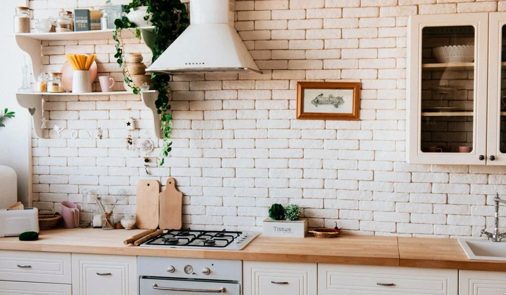 Wooden kitchen worktop with a gas hob, chopping boards and open shelves against a white brick splash