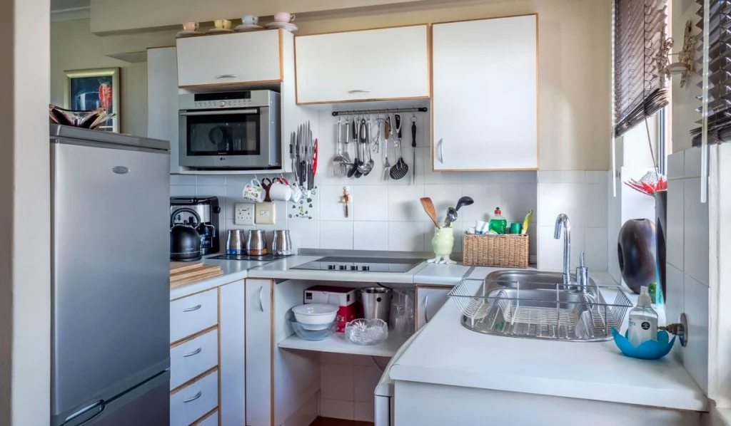 Compact galley kitchen with wall cabinets, a hanging utensil rail and a window over the sink